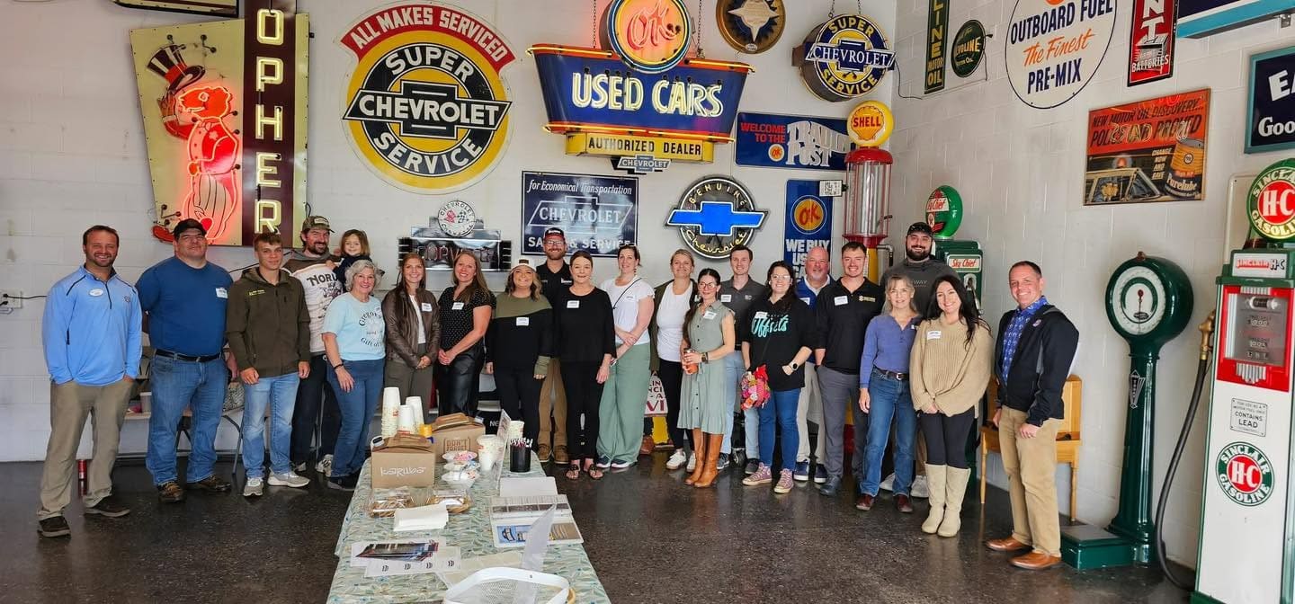 Group photo of about two dozen members in a garage decorated with vintage Chevrolet and gas station signs